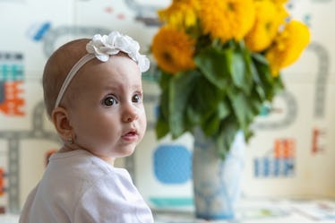 Portrait of a baby girl at nine months old. The child sits on a children's play mat. Sunflowers stan...