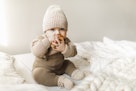 漂亮的男婴穿着棕色的针织衣服，戴着帽子和袜子，甜美地躺在床上。时尚针织……