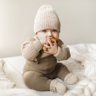 Beatiful baby boy in brown knitted cloths and hat and socks, lying sweetly posed in bed. Trendy knit...