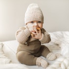 Beatiful baby boy in brown knitted cloths and hat and socks, lying sweetly posed in bed. Trendy knit...