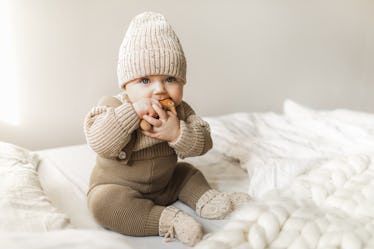 Beatiful baby boy in brown knitted cloths and hat and socks, lying sweetly posed in bed. Trendy knit...