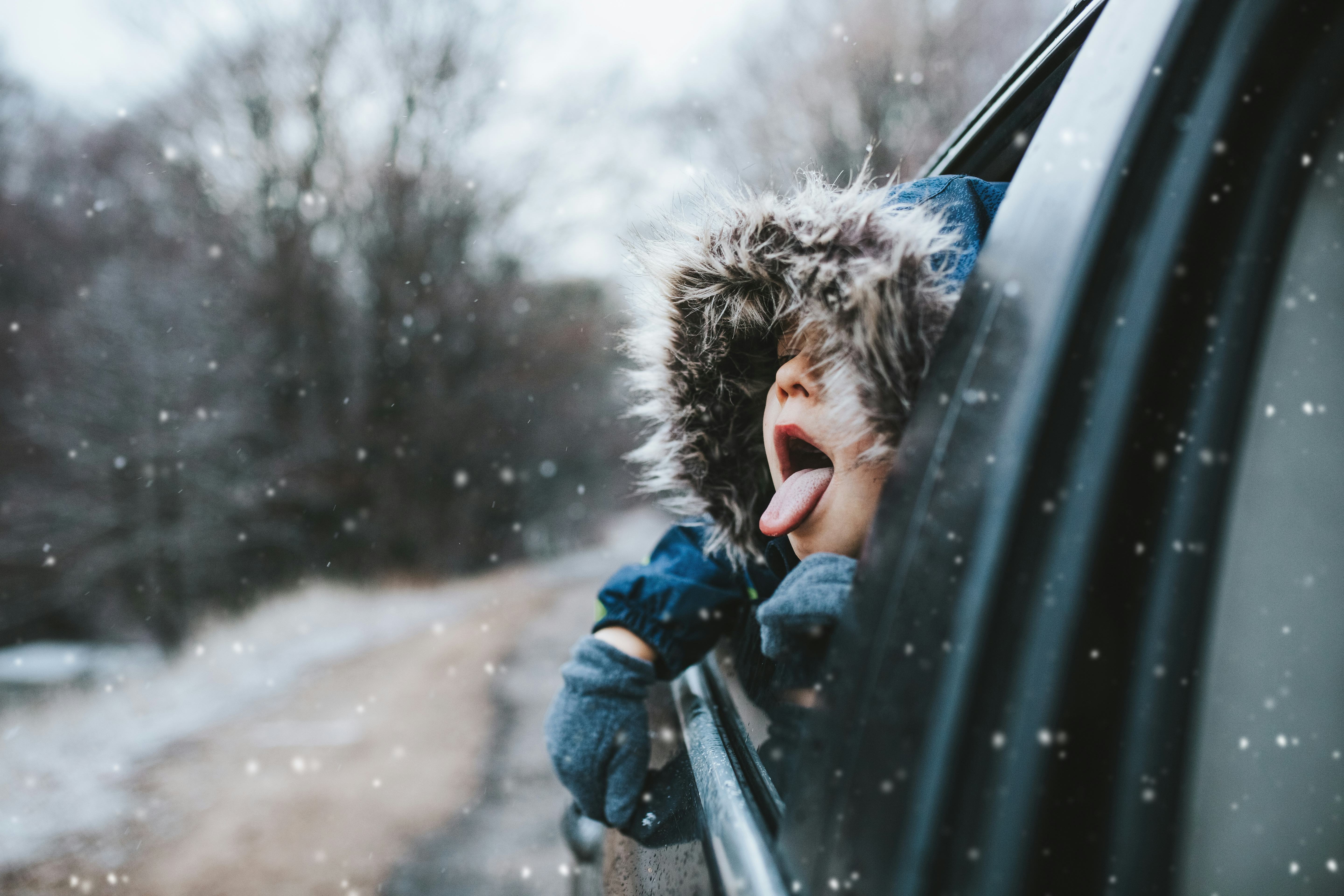 Boy on a road trip sticking his tongue out the window to catch snowflakes, in a story about tips for...