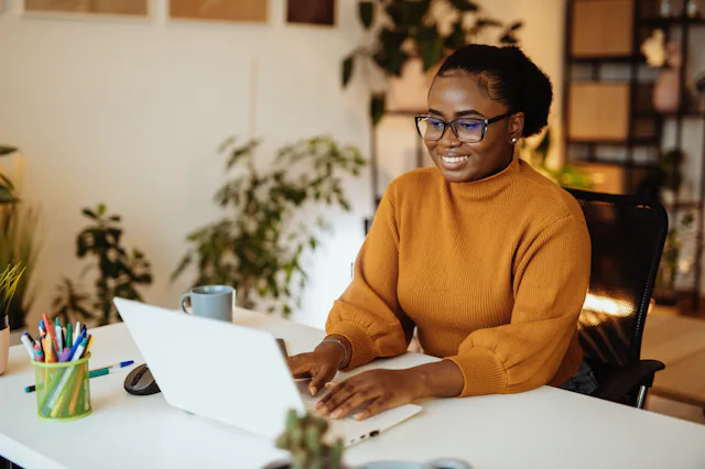 A woman in a yellow sweater with glasses typing on a laptop, showcasing the success forecasted in th...