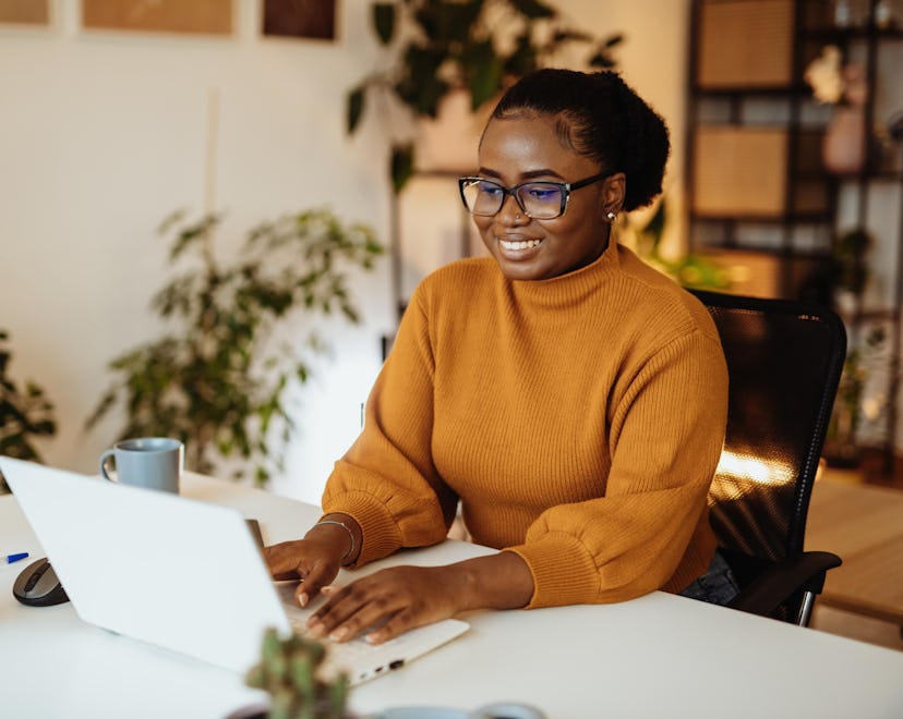 A woman in a yellow sweater with glasses typing on a laptop, showcasing the success forecasted in th...