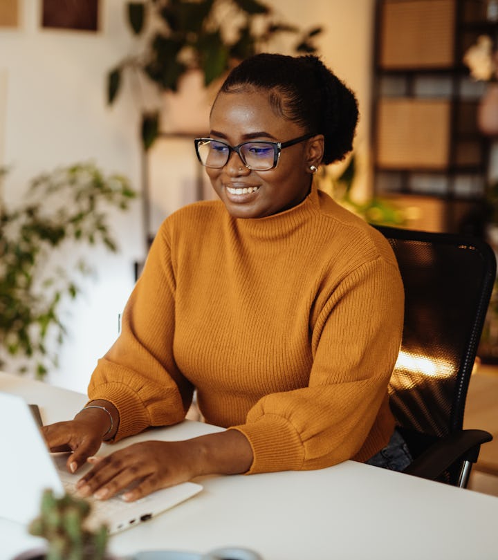 A woman in a yellow sweater with glasses typing on a laptop, showcasing the success forecasted in th...