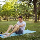 A young adult man performing an exercise on a yoga mat in a public park