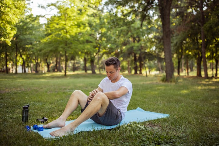 A young adult man performing an exercise on a yoga mat in a public park
