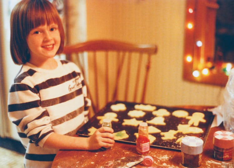 Vintage 1990s child baking Christmas cookies inside domestic kitchen. Happy child is decorating cook...