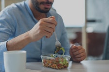 Closeup of the hand of a middle-eastern man using a fork to eat a healthy salad in a glass container...