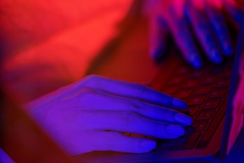 Neon light illuminated hands typing on a computer keyboard