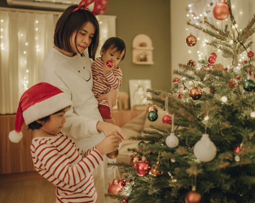 mom holding baby helping her child hang up baby's first christmas ornaments