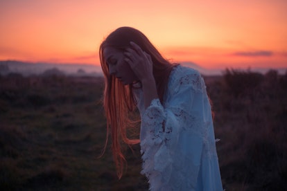 Young woman standing in front of a sunset, knowing her unlucky zodiac sign will have the worst week ...