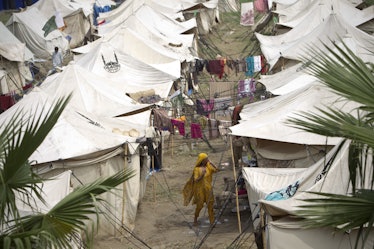 A Pakistani woman displaced by floods walks along a lane between tents set up at a college by the ar...