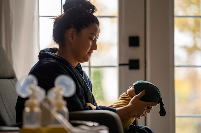 A new mother sitting on a rocking chair in her living room wearing a housecoat holding her newborn b...