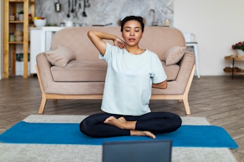 Young African woman practicing yoga at home with laptop