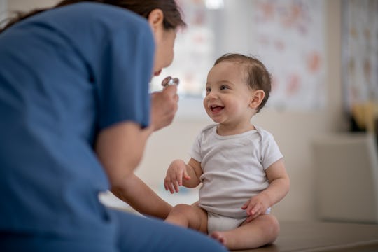 An adorable 8 month old baby is sitting on the examination table during a medical check up. He is sm...