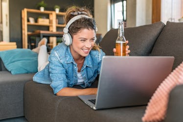 Photo of young woman drinking beer and toasting with friends on a video call, for which she needs Su...