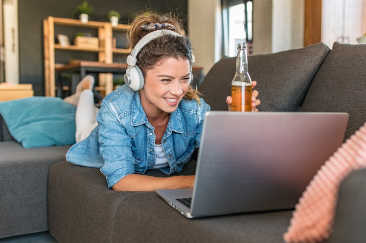 Photo of young woman drinking beer and toasting with friends on a video call, for which she needs Su...