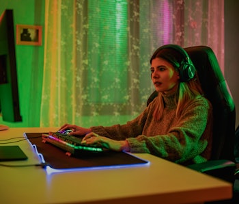 Excited young female Gamer in Headset Playing Online Video Game on Computer at home.