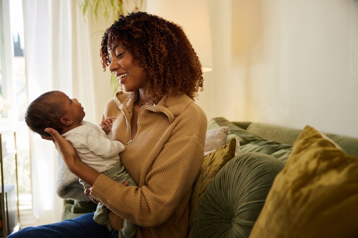 Proud mom smiling down at her adorable baby boy cradled in her arms while sitting on a sofa at home