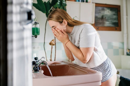 Woman bending over bathroom sink washing her face.