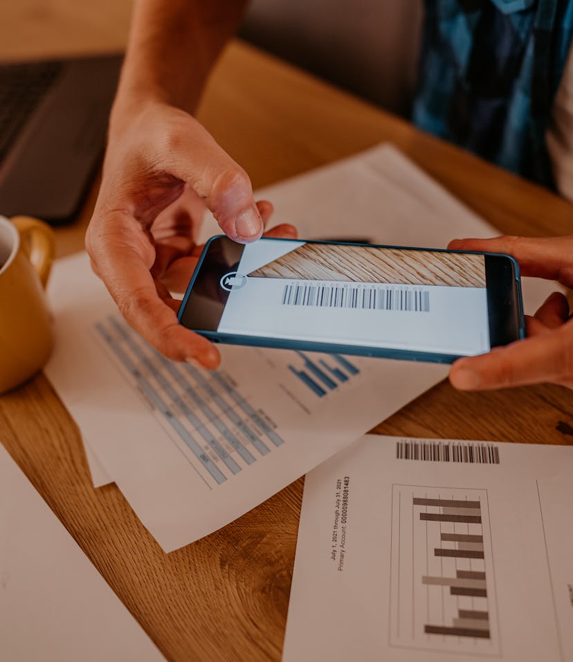 Handsome man paying bills via bar code payments. He is scanning bar code on the bill with his phone.