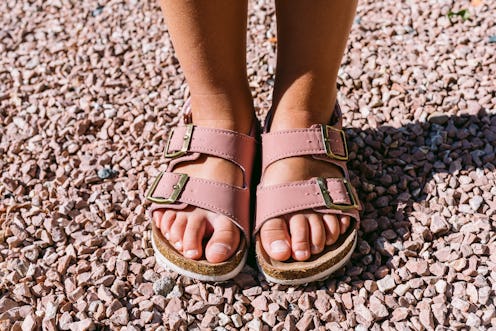 Detail front view of toddler girl feet wearing pink buckle sandals on pink stones in natural light w...