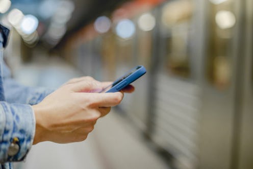 Close up photo of woman's hand holding mobile phone while waiting for the train