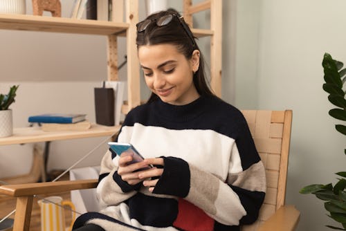 Smiling woman using smartphone at home. Can you see who views your instagram story? Yes, and here's ...