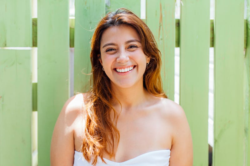 woman smiling on a sunny date in front of a green fence