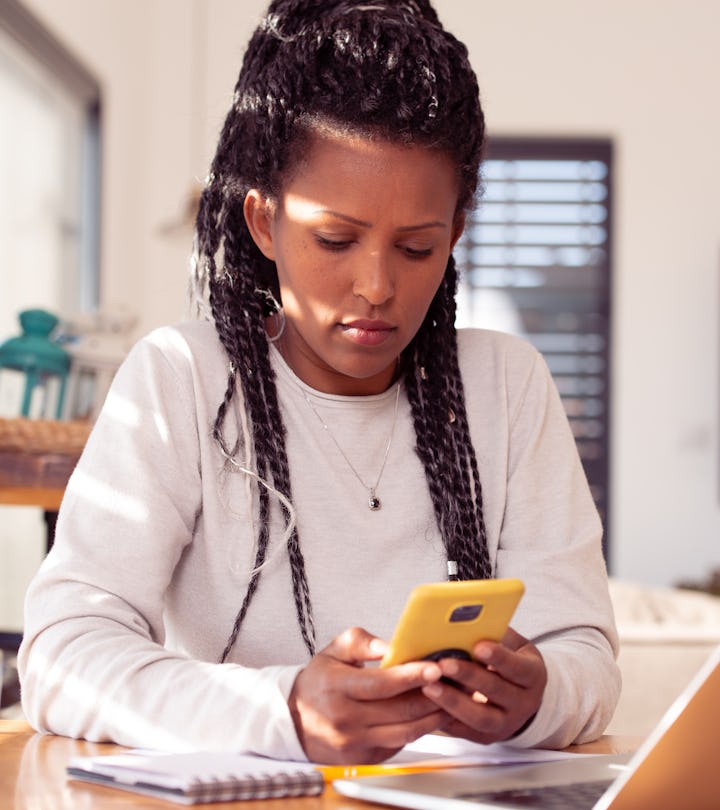 A businesswoman woman using a smartphone and laptop, sitting in the kitchen, drinking coffee. Female...