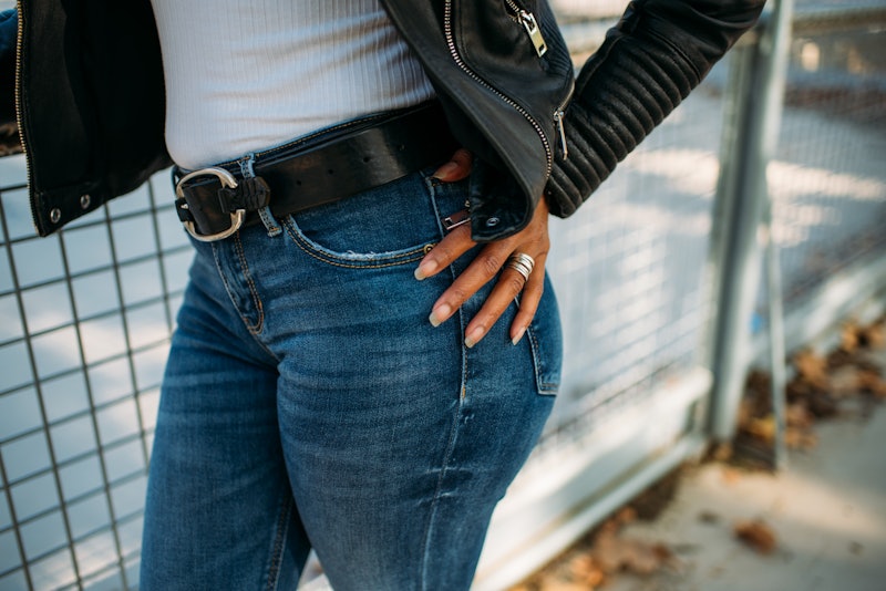 Crop unrecognizable African American female in casual jeans and leather jacket standing with hand on...