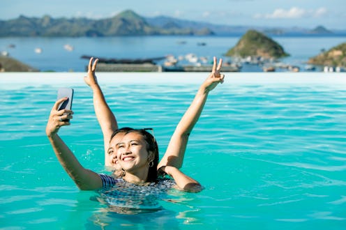 Portrait two young Asian young women swim in pool taking selfie