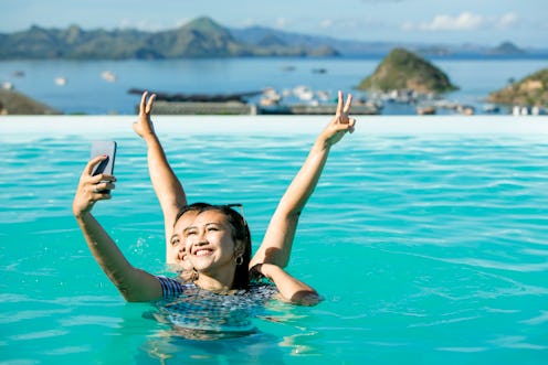 Portrait two young Asian young women swim in pool taking selfie