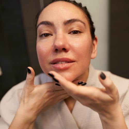 From above female with manicure spreading moisturizing product on neck and looking at camera during ...