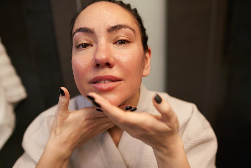 From above female with manicure spreading moisturizing product on neck and looking at camera during ...