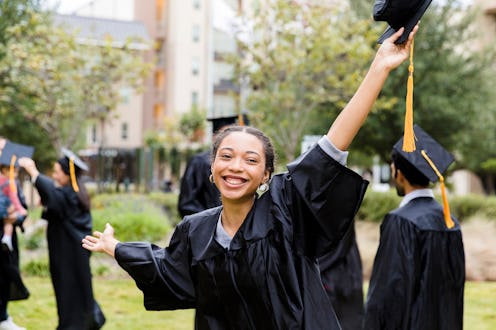 A beautiful female college holds mortarboard up high in celebration after her graduation.