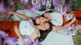 two women smile at the camera as they enjoy a picnic, discuss the zodiac signs who will be most affe...
