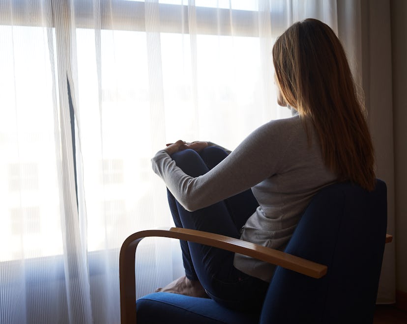 Back view of a sad woman sitting in an armchair looking out the window. Concept of mental health, an...