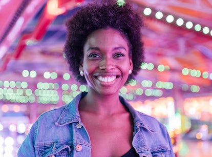 Young woman smiling at a carnival, knowing her lucky zodiac sign will have the best month of March 2...