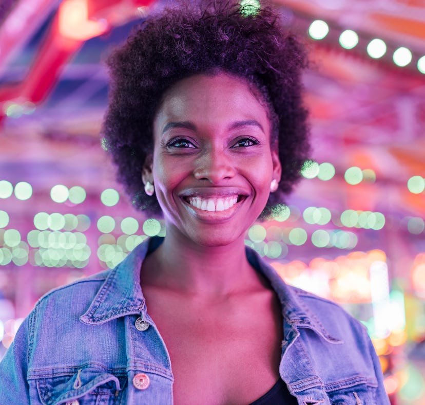 Young woman smiling at a carnival, knowing her lucky zodiac sign will have the best month of March 2...