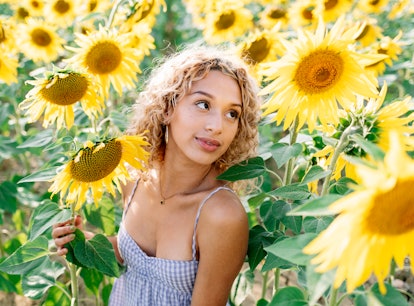 young woman posing in a field of sunflowers as she thinks about how the 2022 spring equinox will aff...