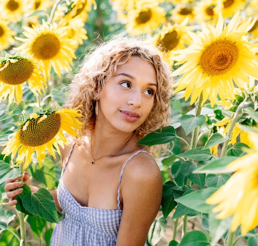 young woman posing in a field of sunflowers as she thinks about how the 2022 spring equinox will aff...