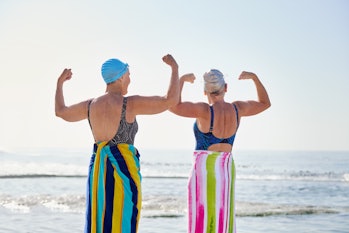 Rear view shot of two active senior women in swimsuits flexing muscles at the beach