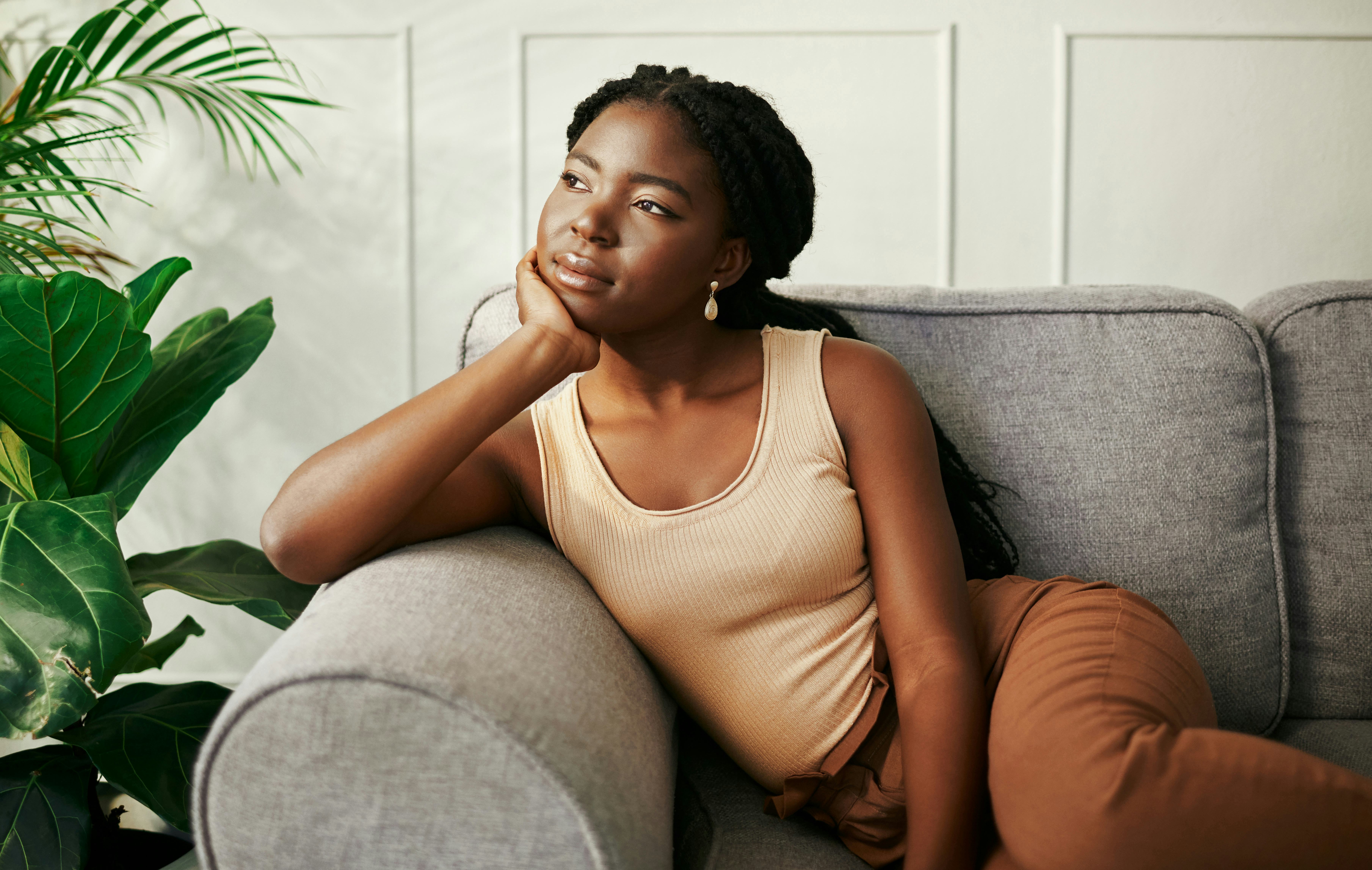 Young woman sitting on a couch stares out into space. Pisces season 2022 is all about dreaming big a...