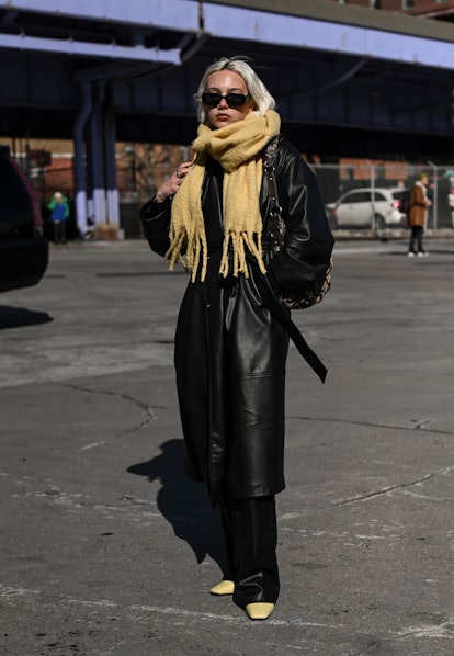 NEW YORK, NEW YORK - FEBRUARY 14: A guest is seen wearing a faux leather coat and yellow scarf outsi...