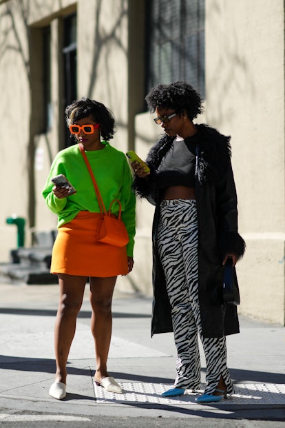 NEW YORK, NEW YORK - FEBRUARY 11: A guest (L) wears neon orange sunglasses, a neon green wool pullov...