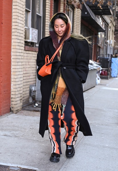 NEW YORK, NEW YORK - FEBRUARY 14: A guest is seen wearing a black coat, orange and black pants outsi...