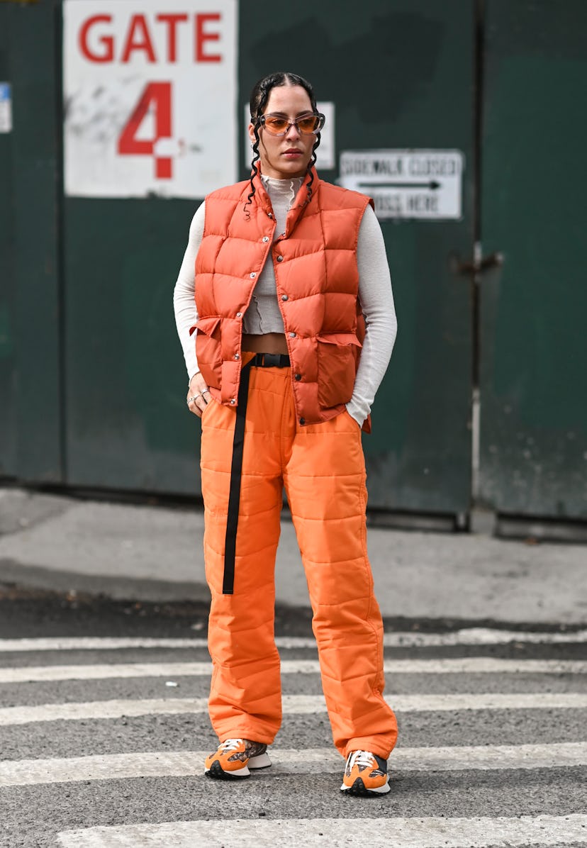 NEW YORK, NEW YORK - FEBRUARY 16: A guest is seen wearing an orange puff vest, white top and orange ...