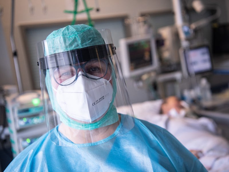 PRODUCTION - 16 February 2022, Hessen, Fulda: An intensive care nurse stands at the bedside of a pat...